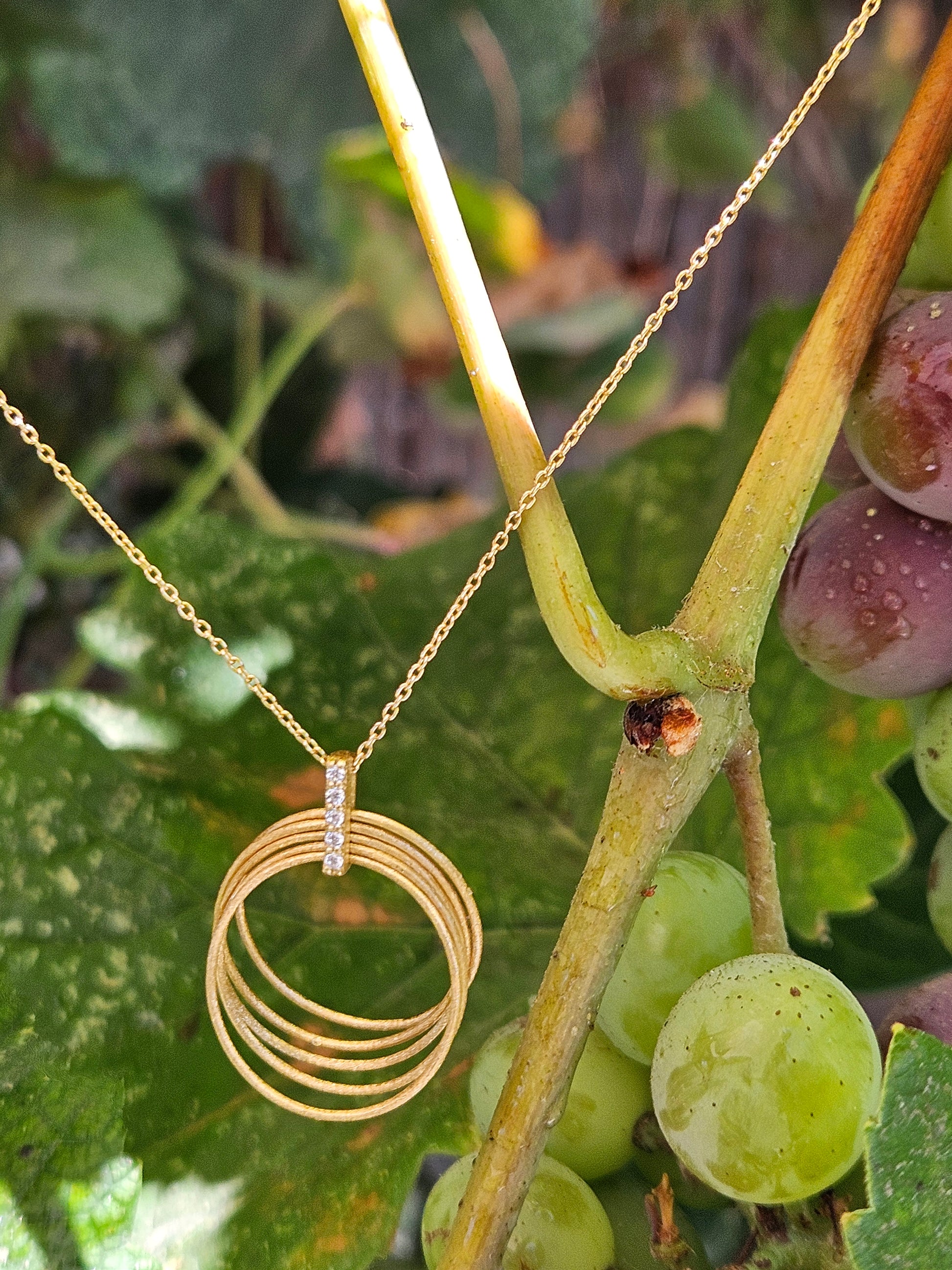 Gold necklace with circular pendant on a grapevine background