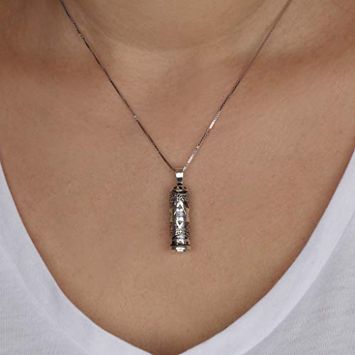 A silver-toned pendant necklace worn on a model's neck, featuring an ornate cylindrical pendant with a central clear stone, set against a white V-neck top.